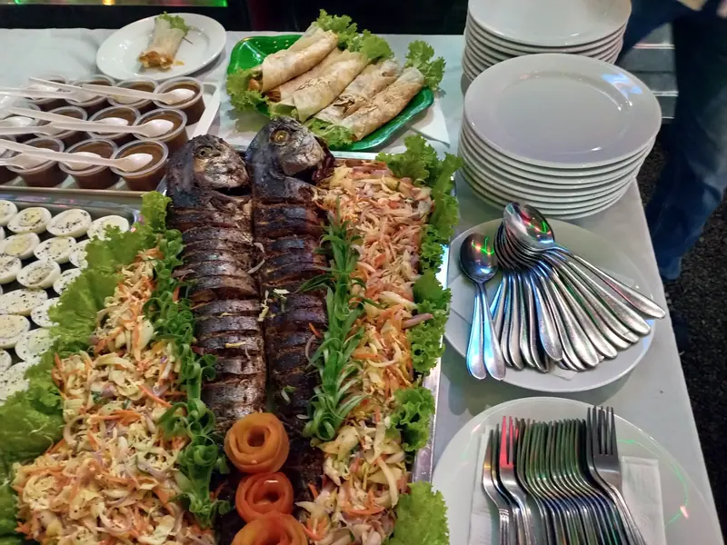 A buffet spread with whole grilled fish, salad, spring rolls and dessert cups