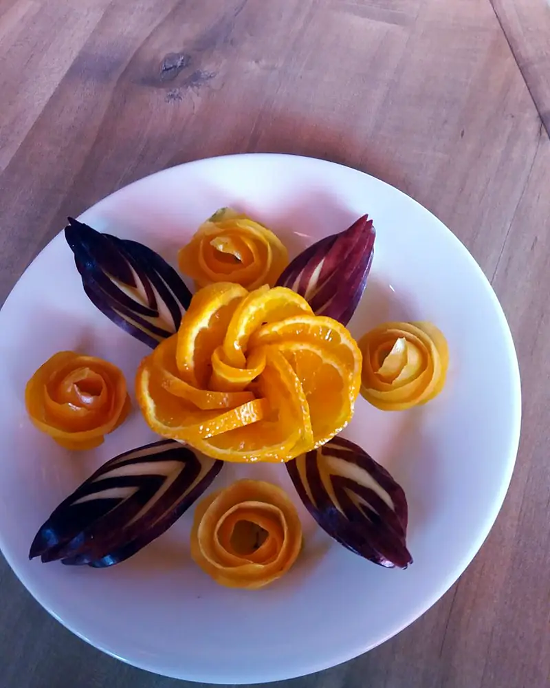 Fresh orange carved into flowers with beetroot leaves on a white plate
